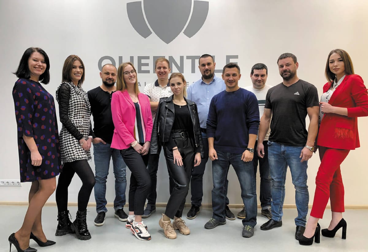 The QUEENTILE team gathered in front of the company logo wall